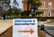 Sign reading Illini Career & Internship Fair with arrow pointing to the right. Illini Union building and fountain in the background.