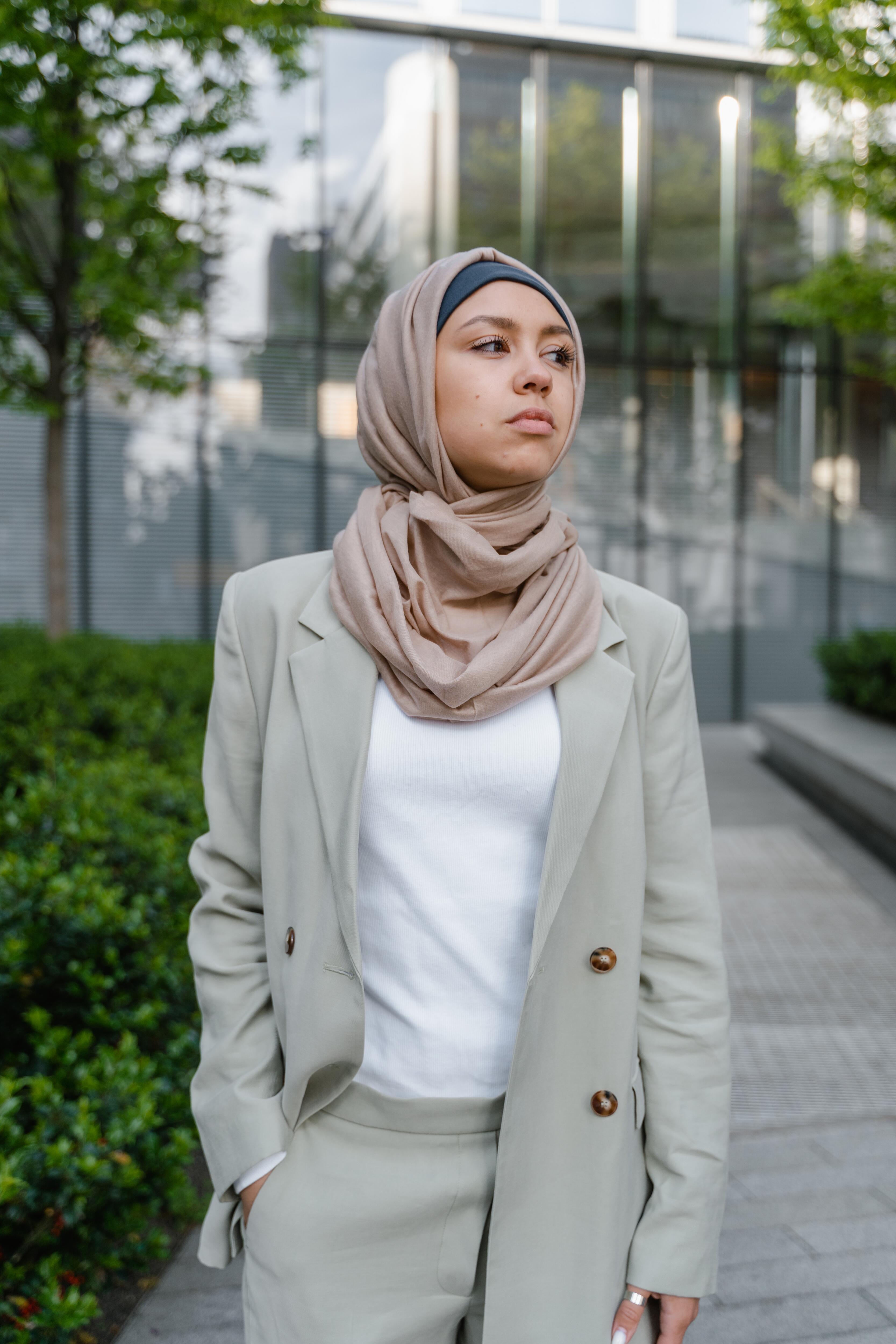 woman in a hijab and taupe-colored suite with white blouse standing outside